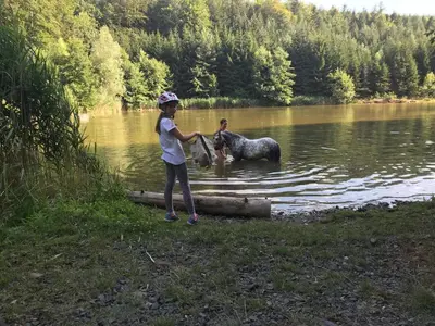 a young girl standing next to a horse in a lake at Bílichov in Bílichov