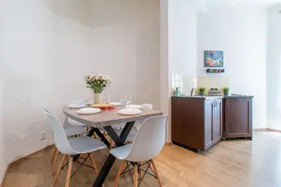 a dining room table with white chairs and a kitchen at Stay Inn Apartments Naplavka in Prague
