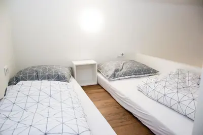 two beds in a bedroom with white walls and wood floors at Sunny Aircon Apartment in the Centre of Slaný in Slaný