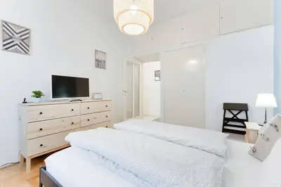 a white bedroom with two beds and a tv on a dresser at Apartment Alex in Prague
