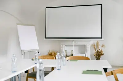 a meeting room with white tables and chairs and a large screen at Na Kmíně in Obříství
