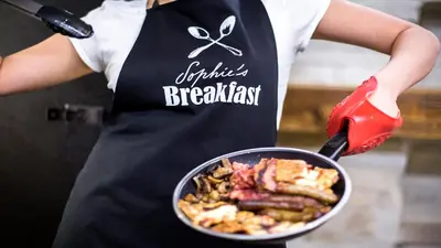 a woman holding a bowl of food with a spatula at Sophie's Hostel in Prague