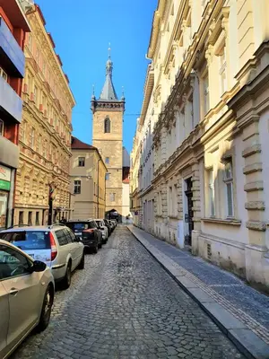 a cobblestone street with a clock tower and cars parked at Reznicka Apartments in Prague