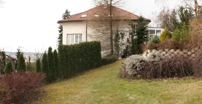 a white house with a hedge in front of a yard at Pension Filip in Prague