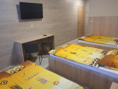a room with three beds and a desk and a television at Penzion Hudebka in Louny