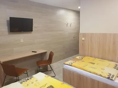 a room with two beds and a tv on a wall at Penzion Hudebka in Louny