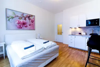 a white room with a bed and a kitchen at Bouquet Apartments in Prague