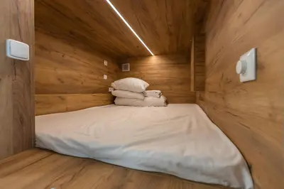 a small bed in a wooden room with towels at Expo capsule Hostel in Prague