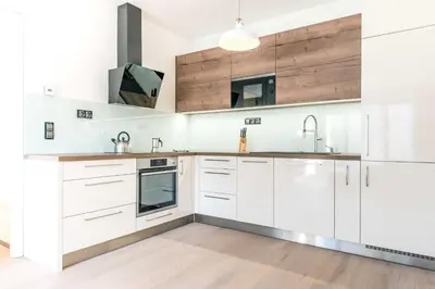 a white kitchen with wooden floors and white cabinets at Quiet & new apartment near city center with garage in Prague