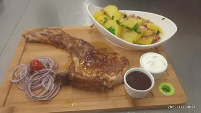 a wooden cutting board with a piece of meat and a bowl of fruit at Malá Svatá Hora - penzion & restaurace in Mníšek pod Brdy