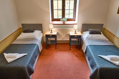 two beds in a room with two tables and a window at Hotel U Lípy in Krušovice