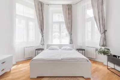 a white bedroom with a white bed and windows at Prague Days - Sunlit Studio near National Museum in Prague
