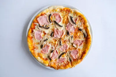 a pizza with ham and mushrooms on a table at Botel Racek in Prague