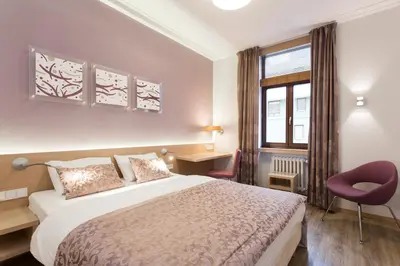 a bedroom with a bed and a chair and a window at Hotel Carol in Prague