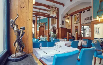 a dining room with tables and blue chairs and a statue at Hotel Paris Prague in Prague