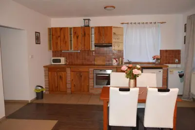 a kitchen with wooden cabinets and a table with white chairs at Bohemica Apartman 3 in Kouřim