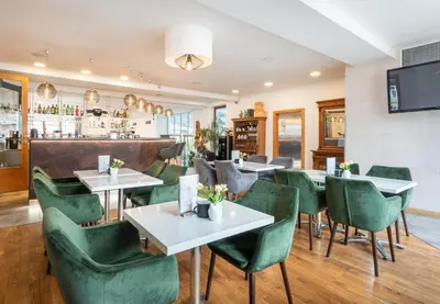 a restaurant with green chairs and tables and a bar at Hotel Troja in Prague