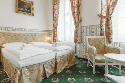 a bedroom with two beds and a chair and a table at Hotel Klarinn Prague Castle in Prague
