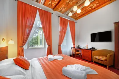 a bedroom with a bed with orange curtains and a desk at Hotel Lippert in Prague