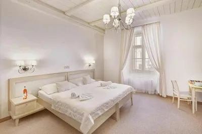 a white bedroom with a large bed and a table at Hotel Lippert in Prague