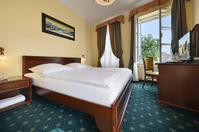 a hotel room with a bed and a desk and a window at Hotel Certovka in Prague