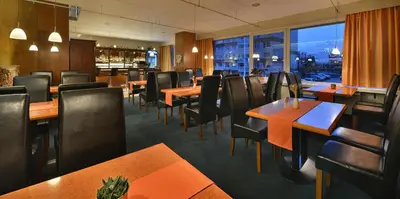 a restaurant with wooden tables and chairs and a large window at Hotel Grand Litava Beroun in Beroun
