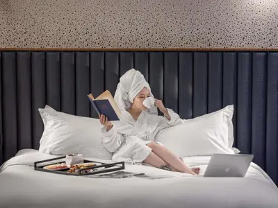 a woman laying in bed with a book and a laptop at Century Old Town Prague - MGallery Collection in Prague