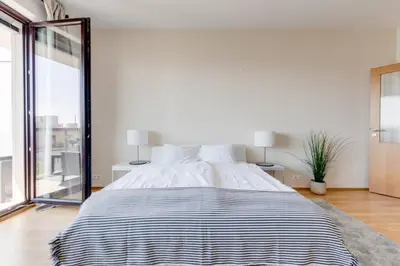 a large bed in a white room with a large window at JT's Apartments Korunní str. in Prague