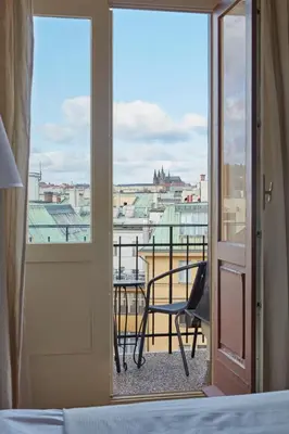 a bedroom with a view of a balcony with a chair at Prague Days - One-bedroom Apartment with View of Castle from Balcony near Wenceslas Square in Prague