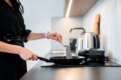 a woman preparing food in a frying pan on a stove at Karl BY ZEITRAUM in Prague