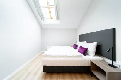 a white bedroom with a bed with purple pillows at Karl BY ZEITRAUM in Prague