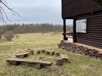 a log cabin with a pile of logs next to a field at Chata s duší in Beroun