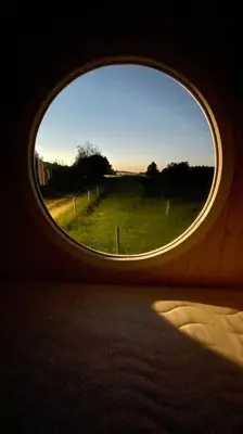 a round window in a room with a view of a field at Glamping - stylová maringotka v srdci Ladova kraje, poblíž hlavního města Prahy in Stříbrná Skalice