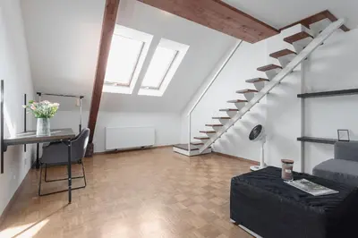 a living room with a black couch and stairs at Bright and Spacious Attic Apartment in Prague