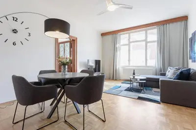 a living room with a table and chairs and a clock at Bright and Spacious Attic Apartment in Prague