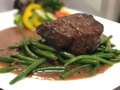 a plate with a piece of meat and green beans at Ubytování u Smrku in Jeneč
