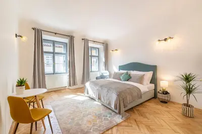 a bedroom with a bed and a table and two windows at Primavera - Castle view apartments in Prague
