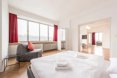 a white bedroom with a large bed and a chair at Merkur apartments in Prague