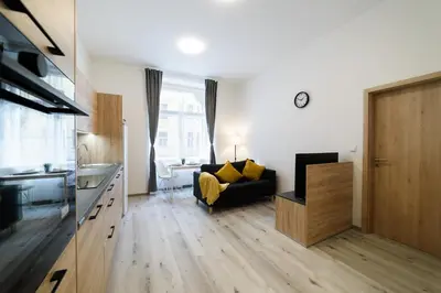 a living room with a black couch and a kitchen at New apartments near Dancing house in Prague